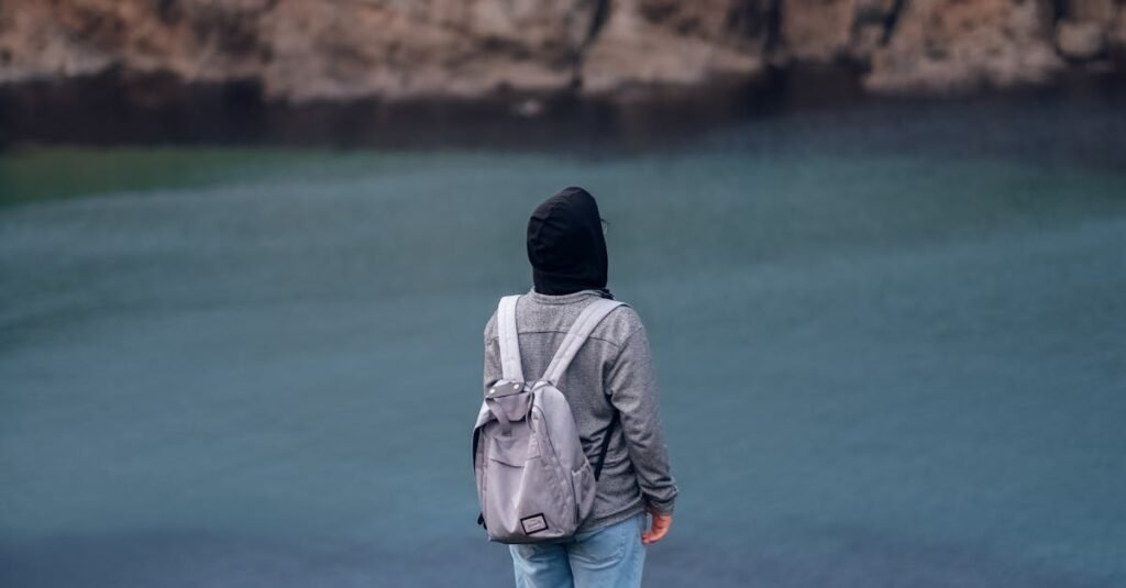 A person with a backpack gazes at a tranquil coastal landscape.